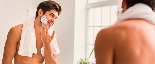 Hombre viéndose al espejo, poniéndose crema en el rostro para cuidar su piel durante el otoño.