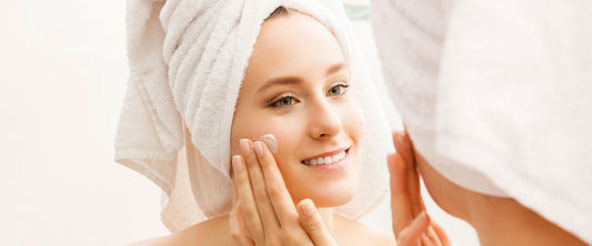Mujer viéndose al espejo, poniéndose crema en la cara.