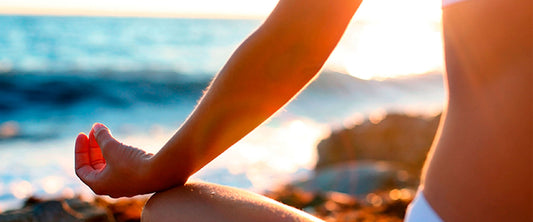 Mujer sentada en la playa en posición de flor de loto.