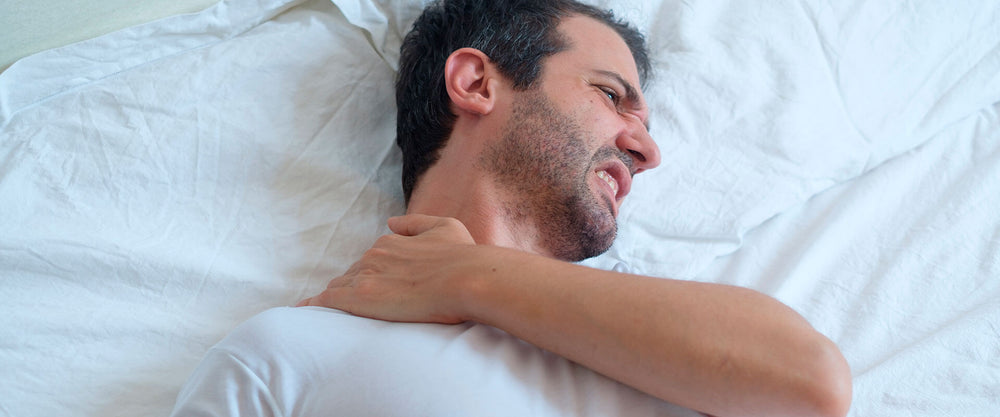 Hombre despertando con dolor de cuello debido a no dormir sobre una almohada soñare.