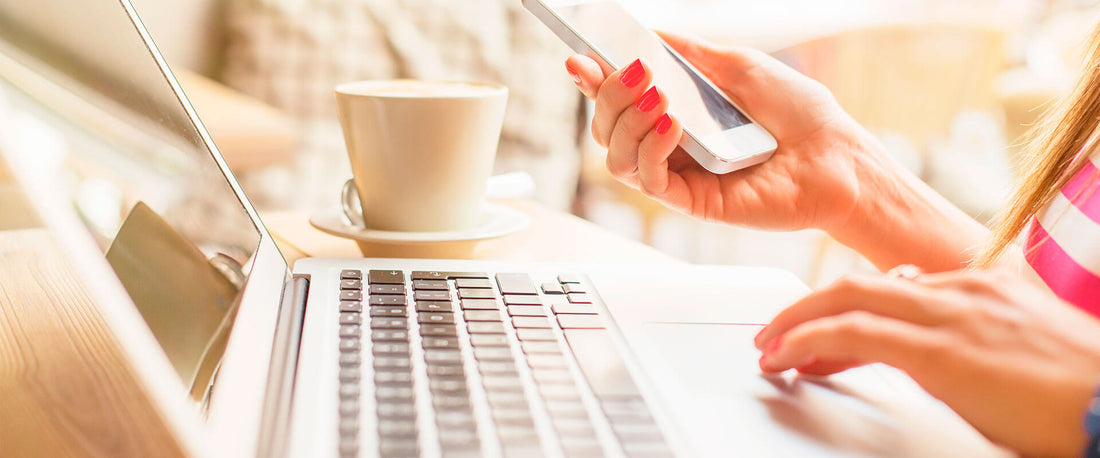 Manos de mujer sujetando un celular y tecleando una computadora para comprar durante el Buen Fin.