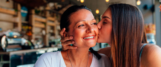 Hija dándole un beso a su mamá en la mejilla.
