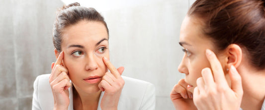Mujer viéndose frente al espejo y tocándose las bolsas debajo de los ojos.