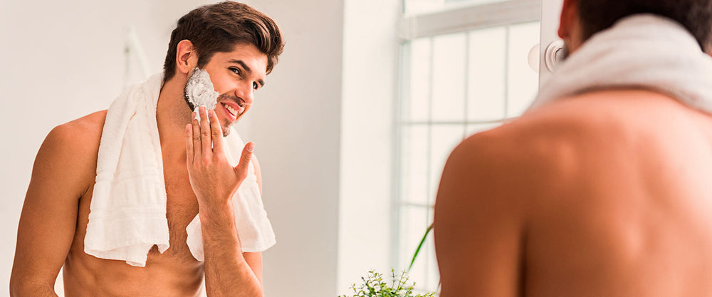 Hombre viéndose al espejo, poniéndose crema en el rostro para cuidar su piel durante el otoño.