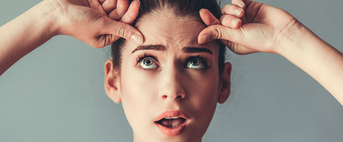 Mujer en sus treintas, estirando la piel de su rostro para evitar las arrugas.