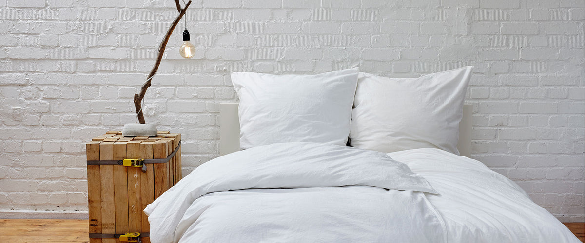 Habitación con ropa de cama color blanco y buró de madera.