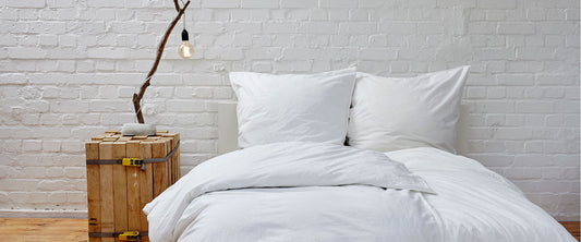 Habitación con ropa de cama color blanco y buró de madera.