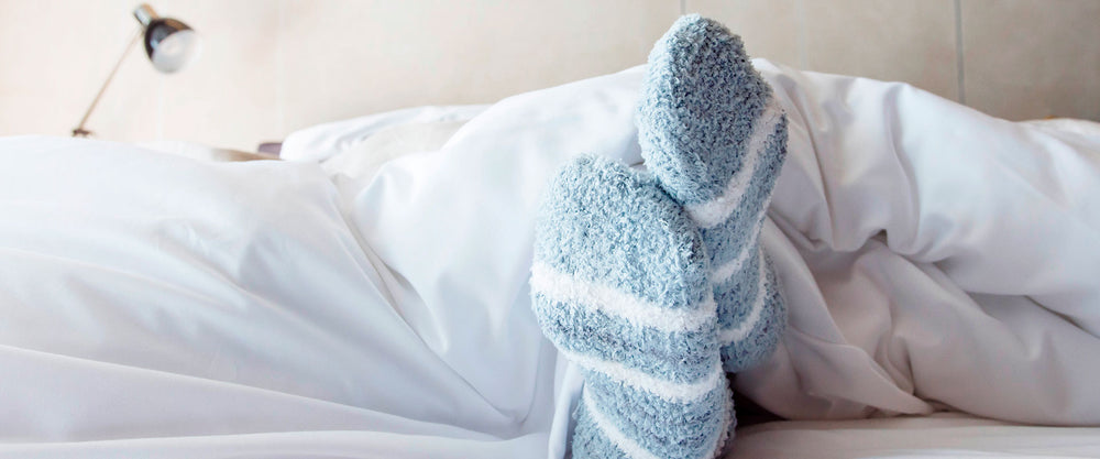Hombre acostado en su cama, usando calcetines de lana para el frío.