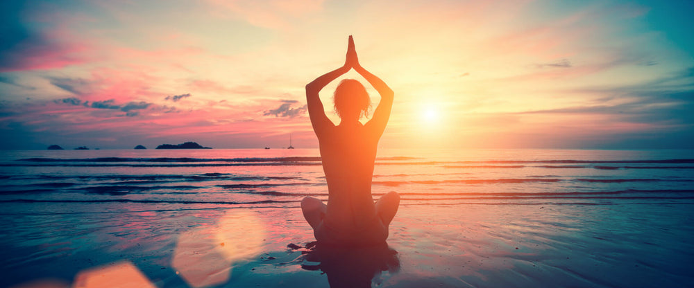 Mujer haciendo yoga al amanecer junto al mar